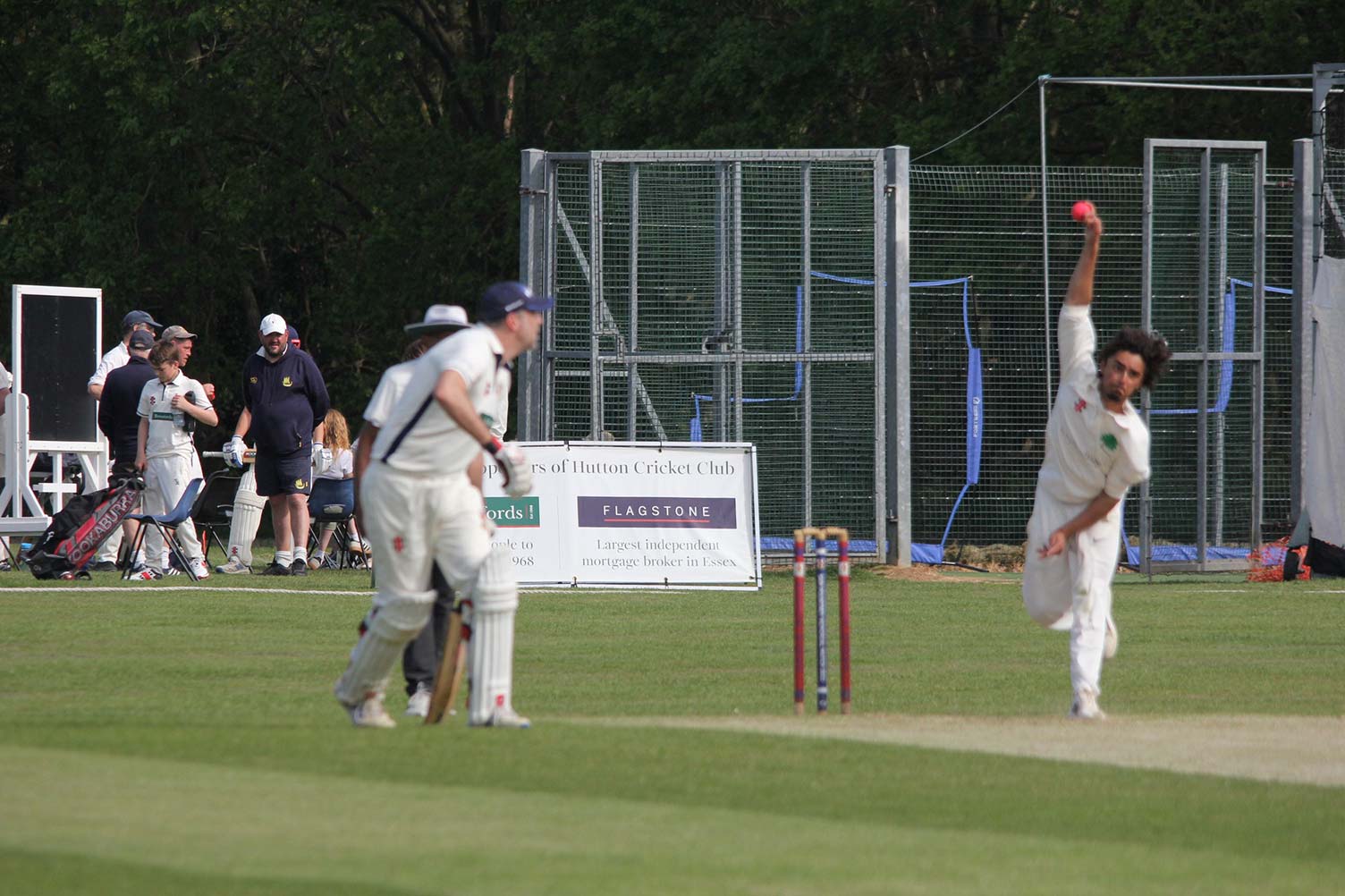 A bowler prepares to deliver a ball while the non-striker and spectators look on