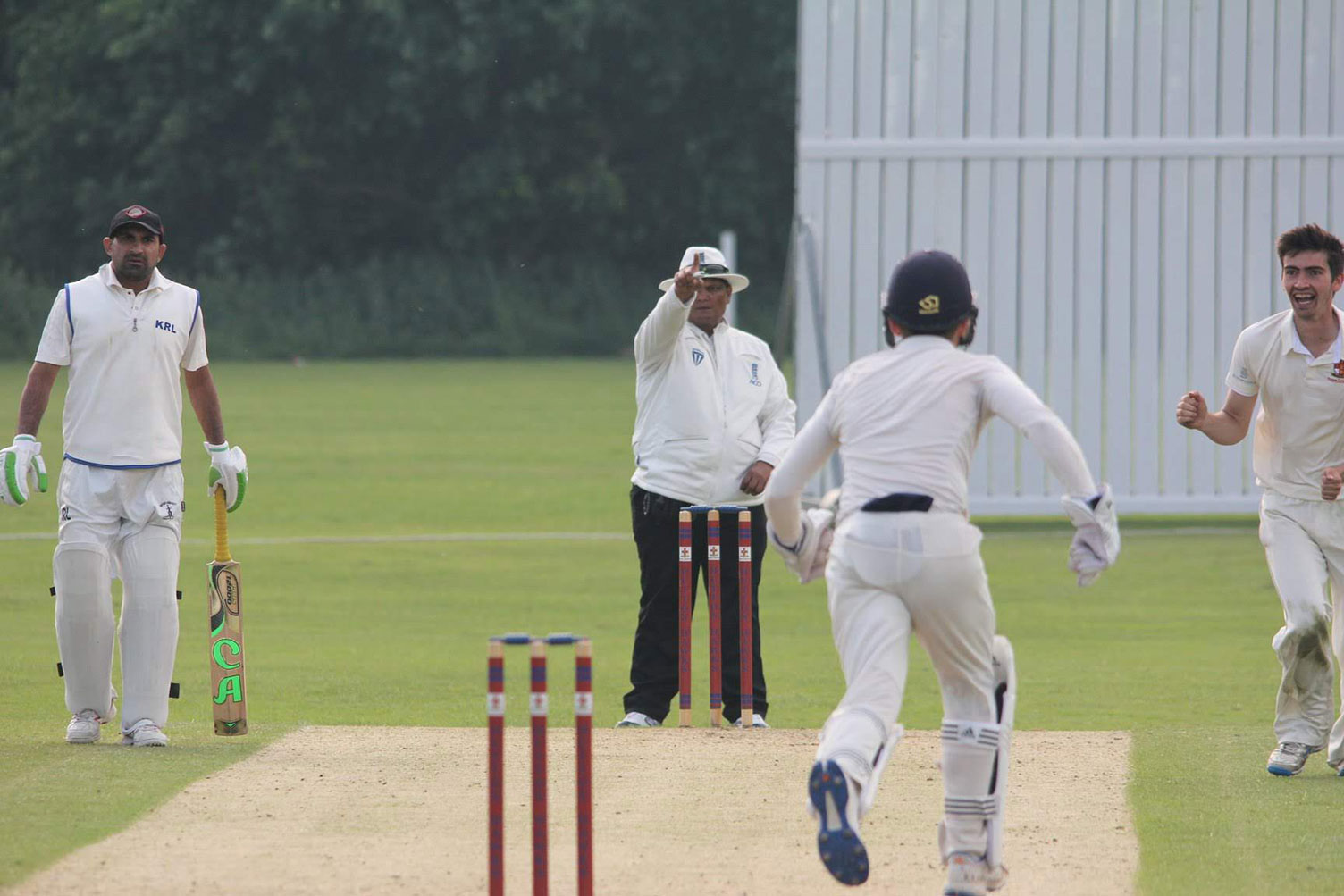 An umpire signalling a dismissal as a bowler and wicketkeeper celebrate