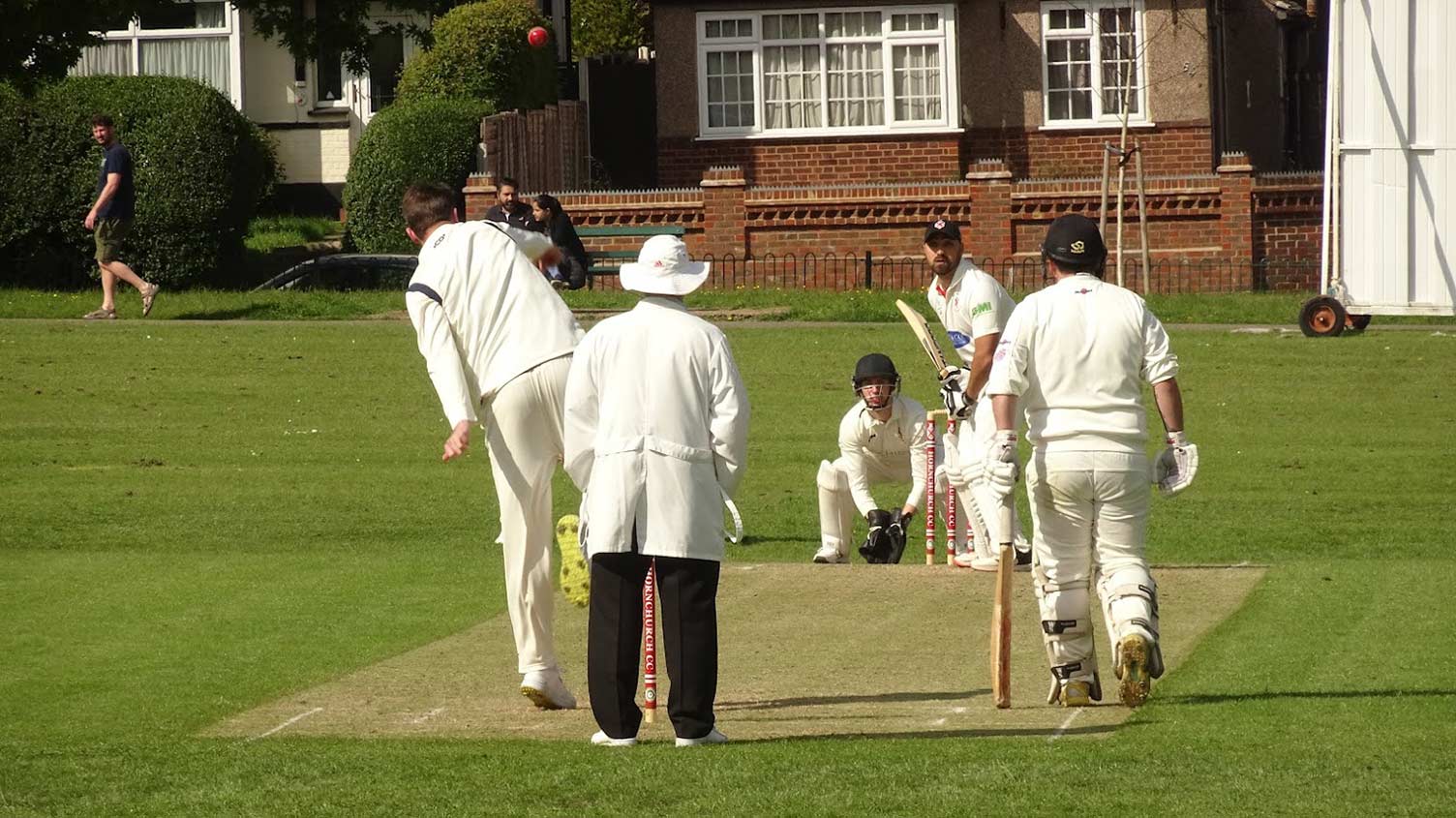 An off spinner delivering the ball to a batter with a wicket keeper standing up to the stumps. The umpire and non-striker watch on.