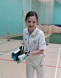 picture of a junior player in cricket whites wearing wicket keeping gloves in an indoor cricket environment